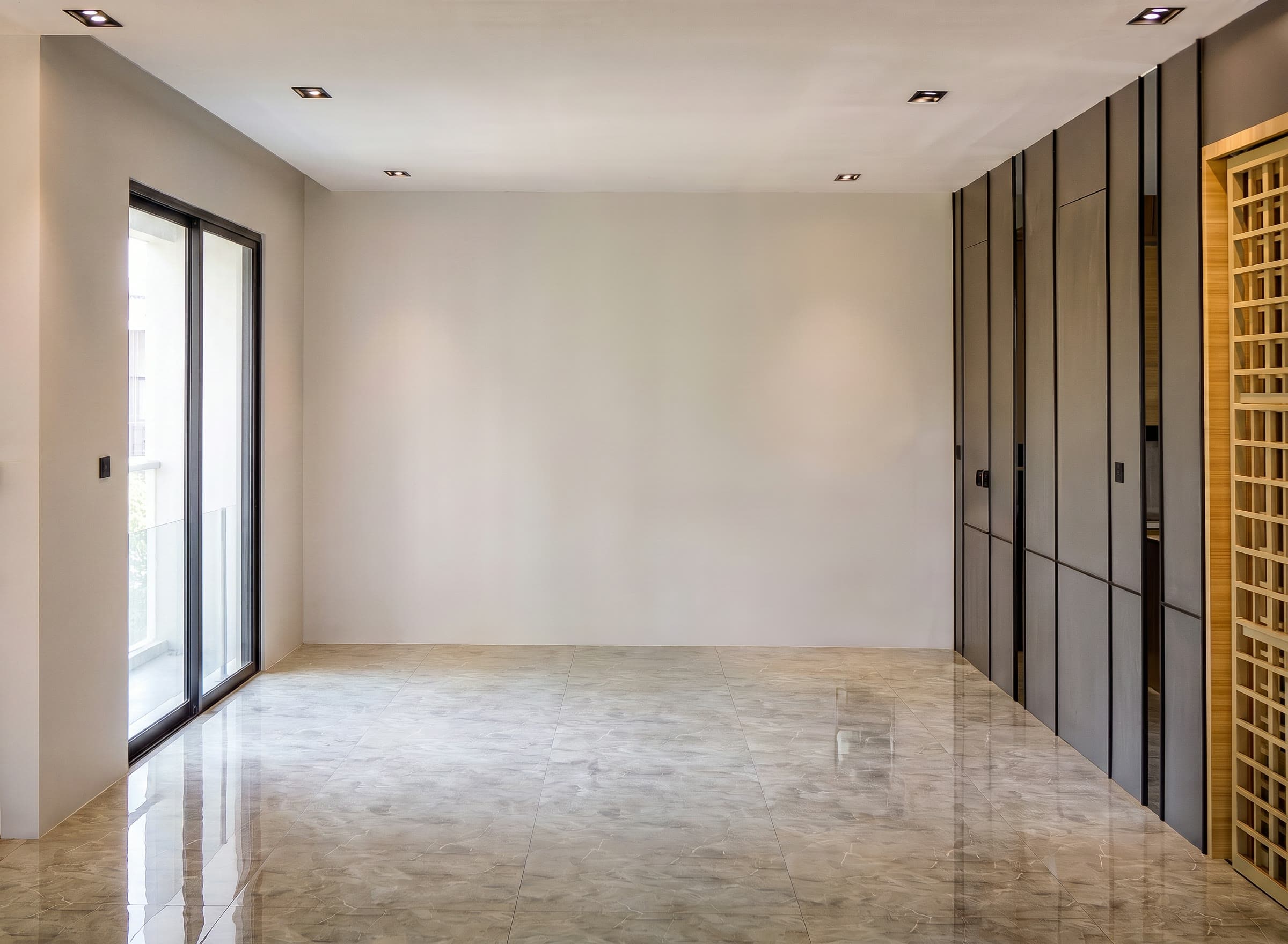 Ambiente vazio com piso de mármore polido, armários embutidos cinza escuro e painel de treliça de madeira