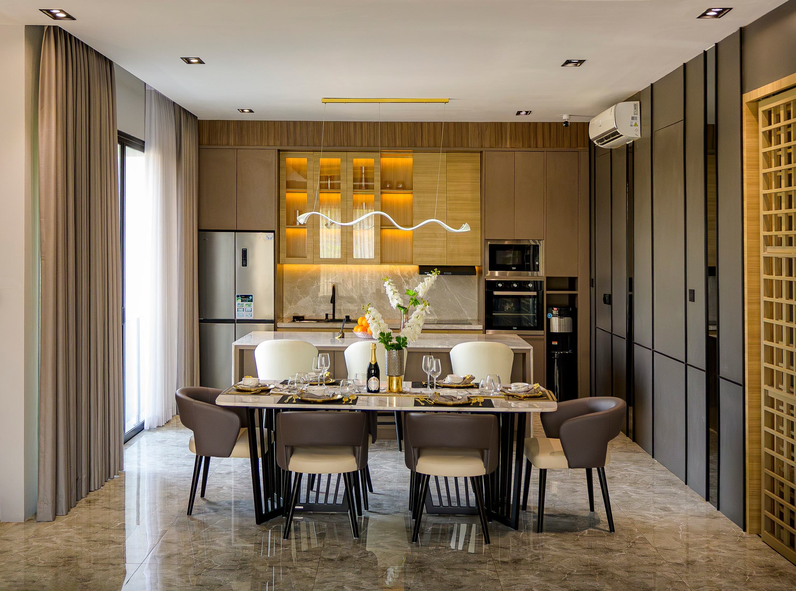O mesmo ambiente com mesa de jantar posta para seis e cozinha moderna ao fundo, com marcenaria de madeira, ilha e eletrodomésticos embutidos