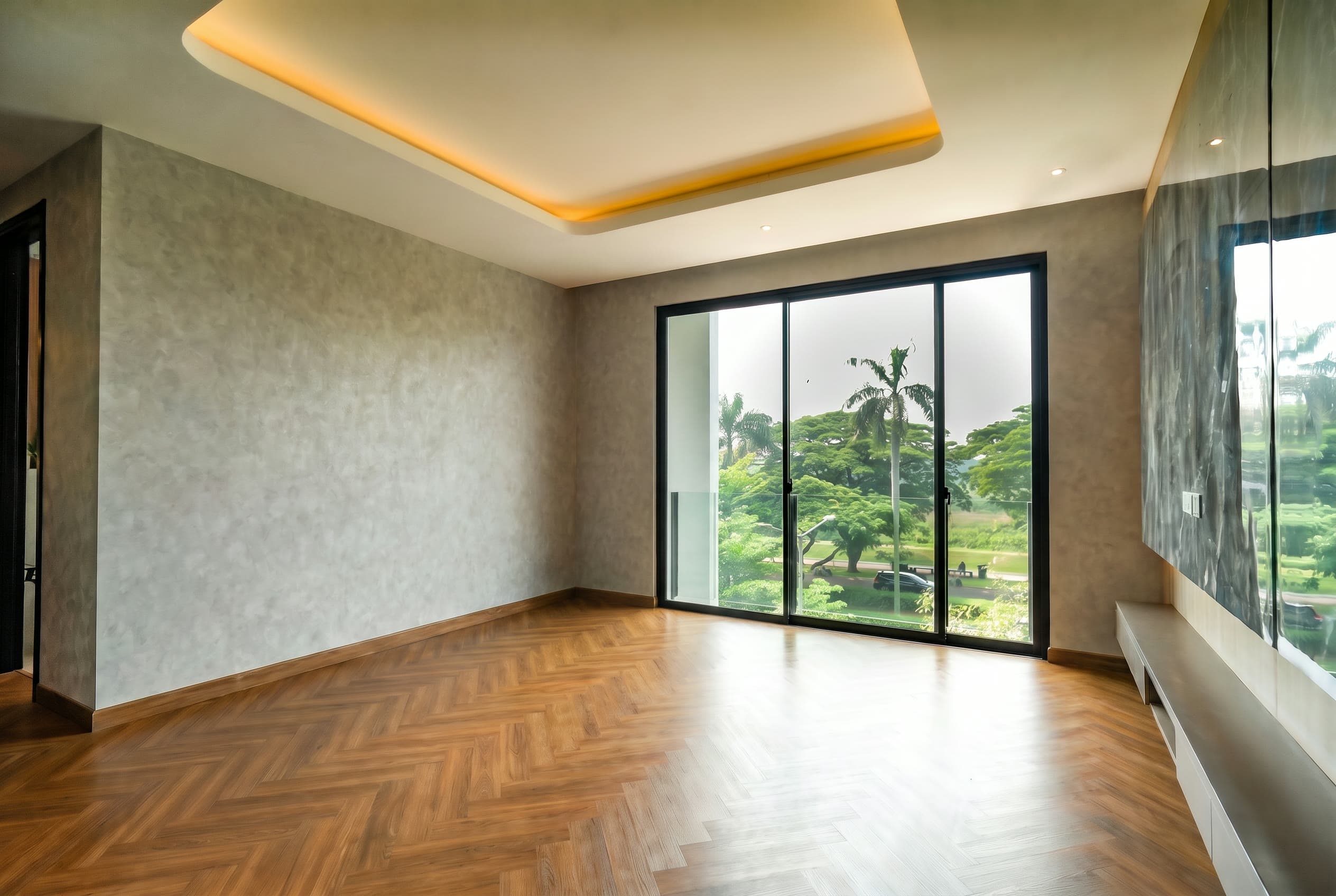Quarto de casal vazio, com piso de madeira em espinha de peixe, porta de correr de vidro para a varanda e vista de árvores