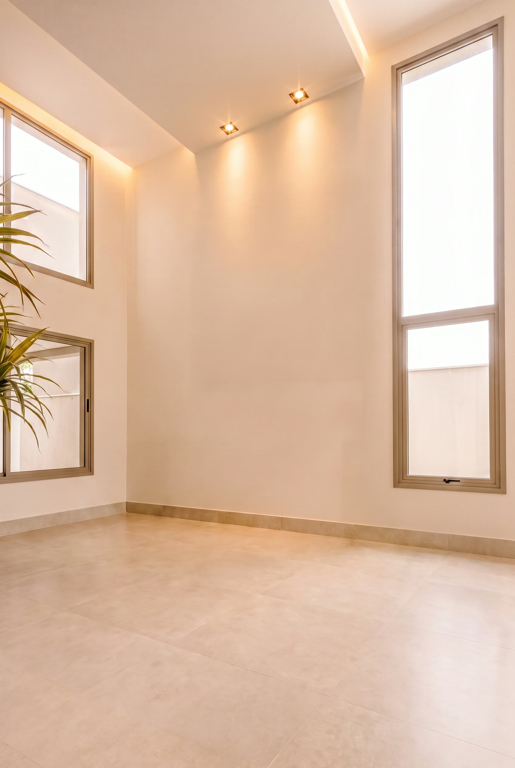 Sala vazia de pé-direito alto, com duas janelas verticais altas e piso claro