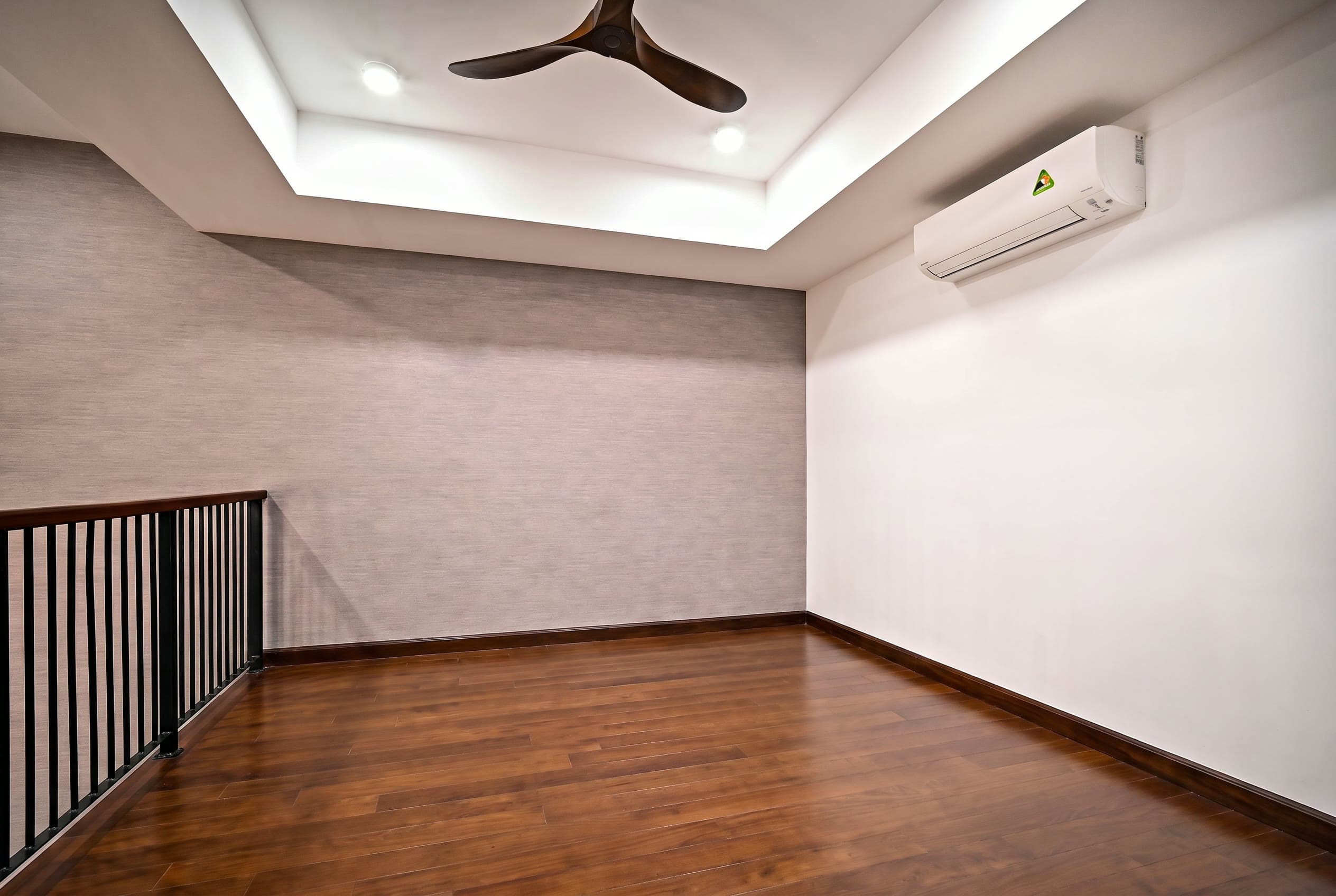 Sala de estar vazia, com piso de madeira escura, papel de parede cinza texturizado, ventilador de teto e guarda-corpo de escada em ferro preto